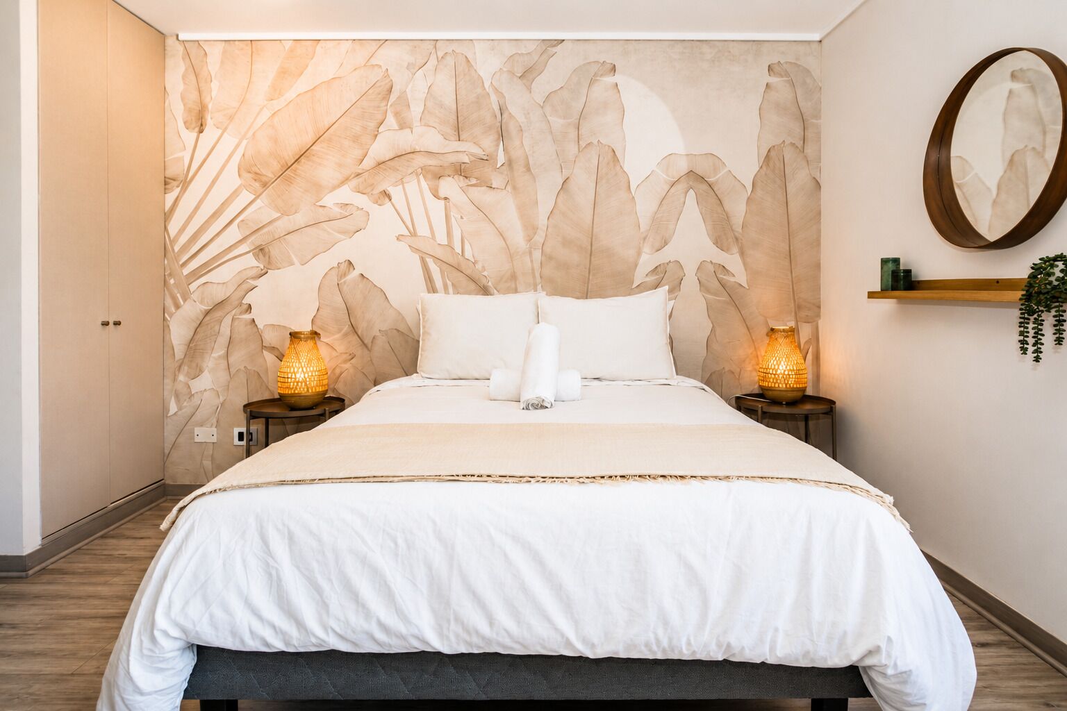 Une chambre à coucher avec un grand lit, deux lampes de chevet, un miroir fixé au mur et une étagère avec une plante.
