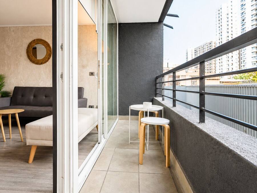 A modern apartment with a balcony, a sofa, two tables, and a potted plant.