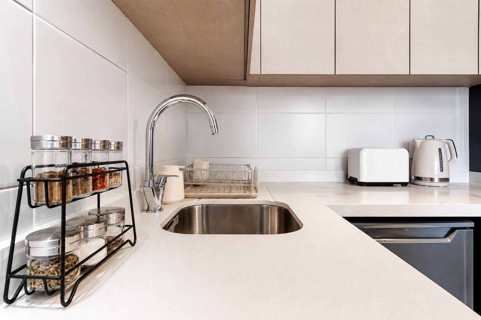 A modern kitchen with a stainless steel sink, a black spice rack, a toaster, and a kettle.