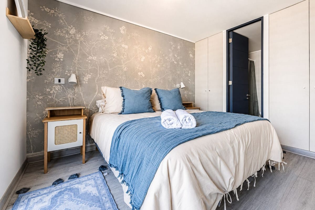 A bedroom with a bed, bedside tables, a wardrobe, a hanging plant, and a patterned rug.