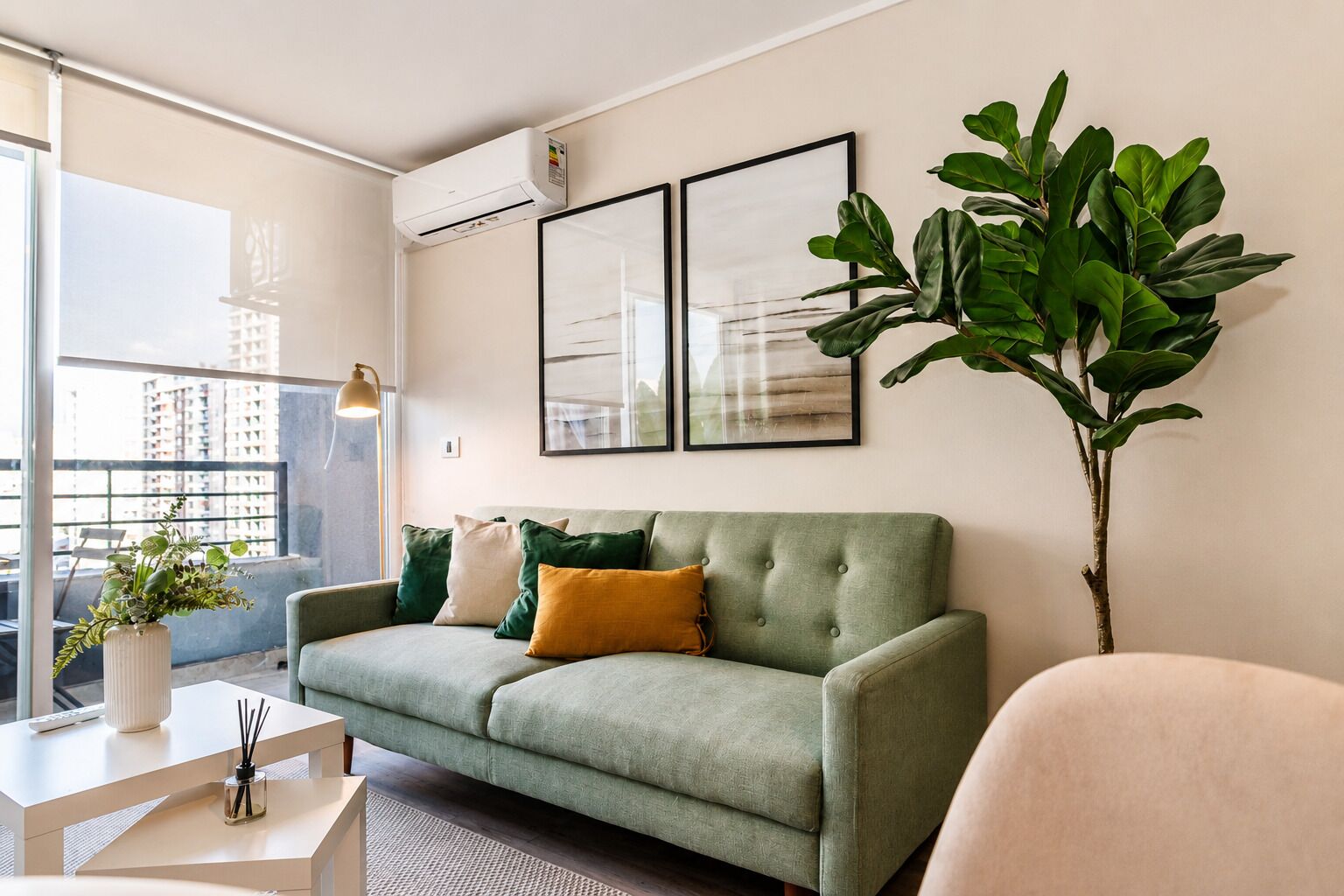 A modern living room with a green sofa, a potted plant, and two framed artworks on the wall.