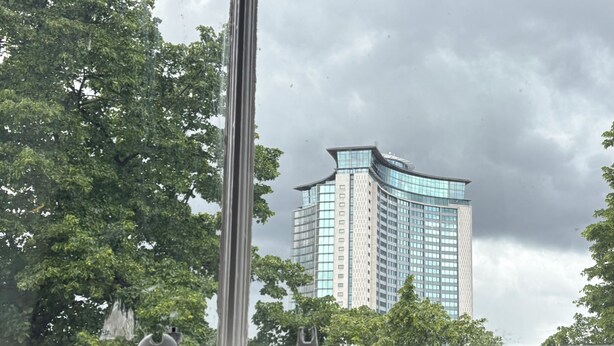 Un edifici alt d'un disseny modern, envoltat de vegetació verda abundant.