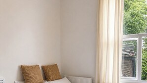 Un llit ben fet amb roba de llit blanca i dos almoinals marrons, una finestra amb cortines beix i un radiador a la paret.