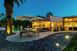 Un'area patio con tavolo e sedie, un ombrellone grande e una piscina.