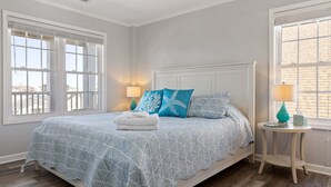 Un dormitorio con una cama, dos lámparas de noche, una mesita redonda y una ventana con persianas.