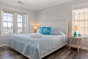A bedroom with a bed, two bedside lamps, a small round table, and a window with blinds. - Steps to beach | Ocean Views | Beach Gear (Carolina Beach)