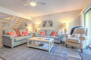 Ein Wohnzimmer mit einer Couch, Sesseln, einem Couchtisch und einer Treppe.