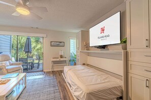 Ein Schlafzimmer mit einem Bett, einem an der Wand befestigten Fernseher, einem Schreibtisch und einem Stuhl.