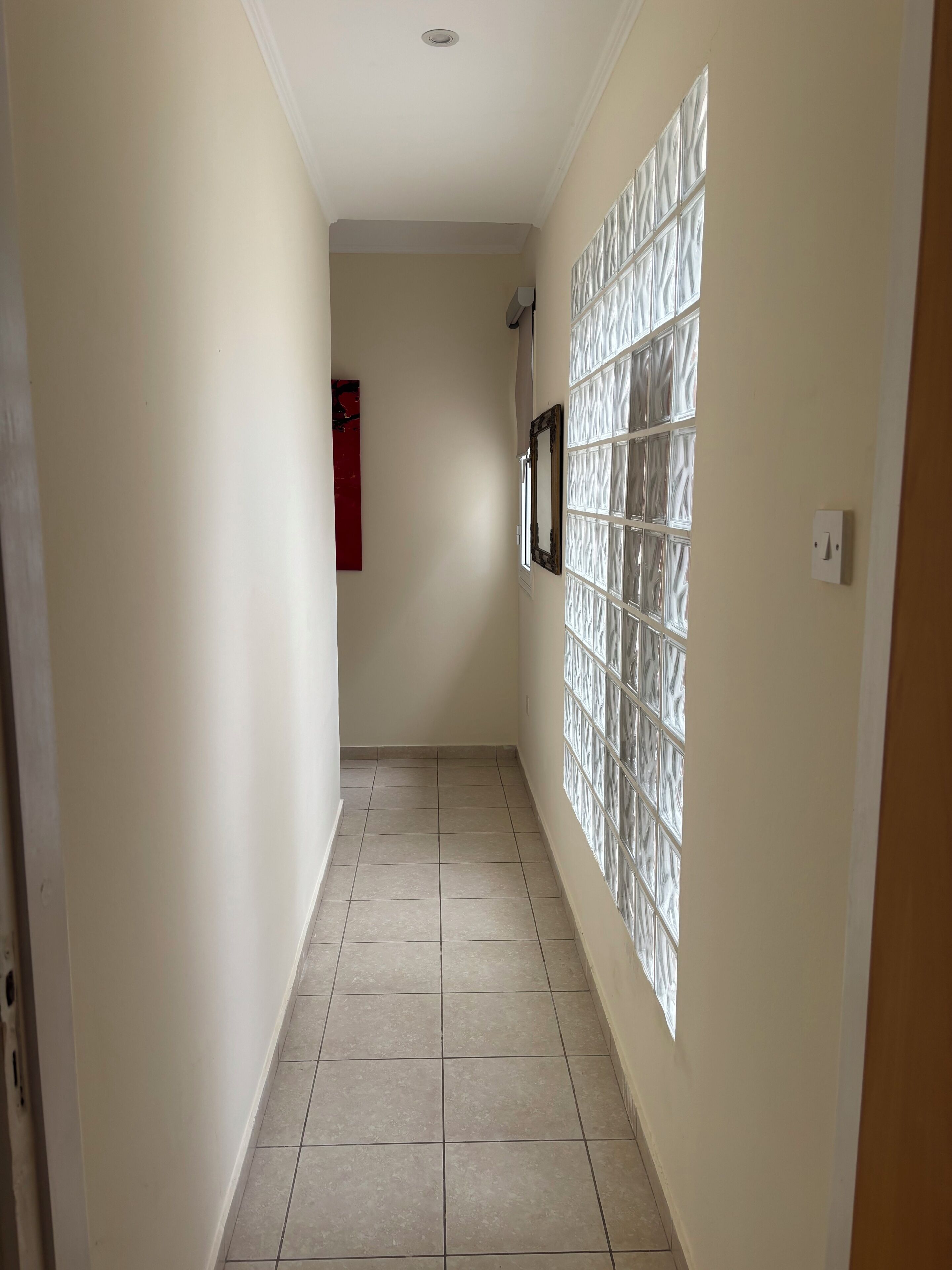 A hallway with a tiled floor, a wall-mounted light switch, and a framed picture.