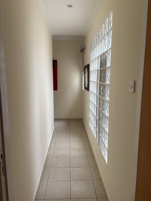 A hallway with a tiled floor, a wall-mounted light switch, and a framed picture. - RELAX IN A PRIVATE 3 BEDROOMS BUNGALOW WITH SWIMMING POOL. (Paphos)