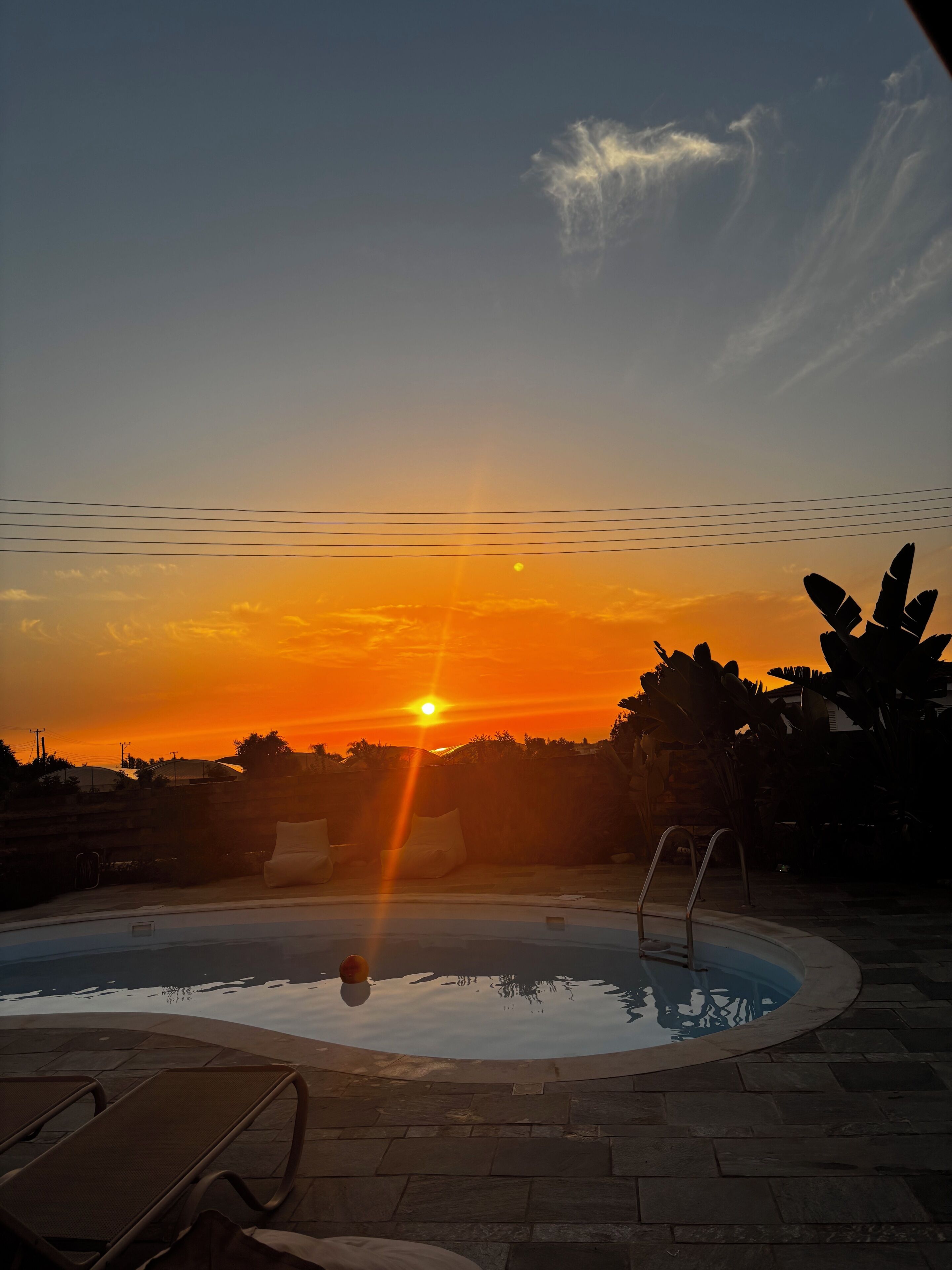 A swimming pool with lounge chairs and a sunset in the background.