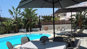 A poolside area with a round table and chairs, a large umbrella, and a pool. - RELAX IN A PRIVATE 3 BEDROOMS BUNGALOW WITH SWIMMING POOL. (Paphos)