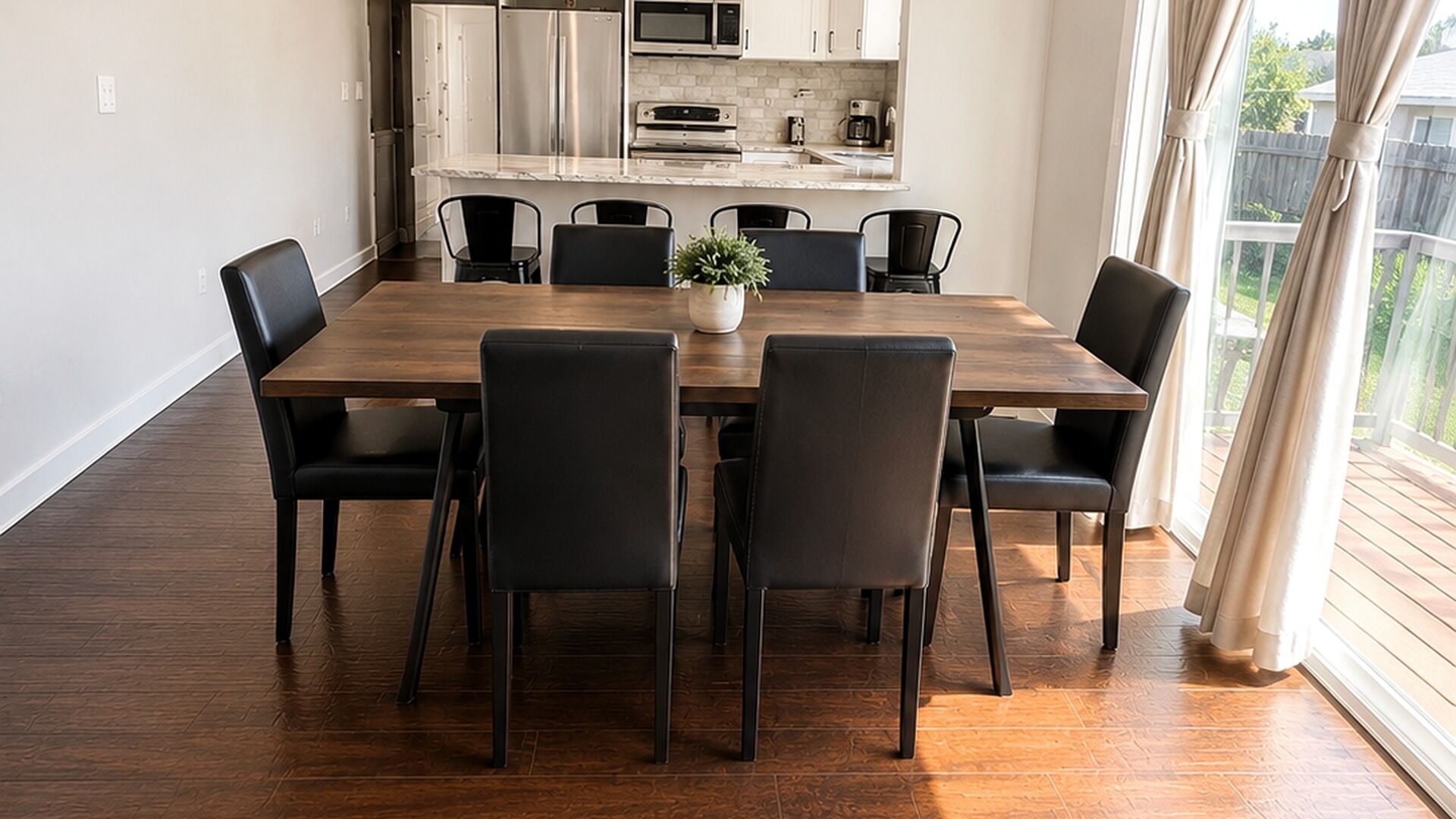 Een eetgedeelte met een houten tafel en zwarte stoelen, een potplant en een keuken op de achtergrond.