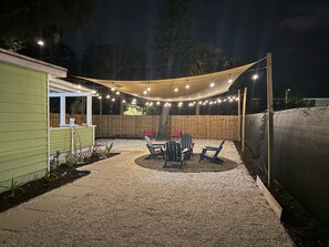 Un patio con mesa y sillas, una cerca de madera y luces colgantes.