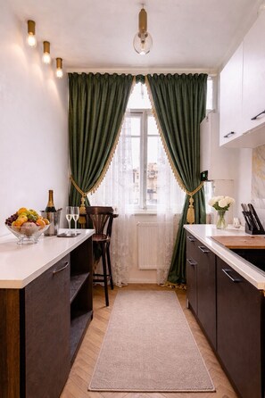 A kitchen with a wooden countertop, a fruit bowl, a bottle, and a vase with flowers. - Tbilisi Legend – Rustaveli 37 (T'bilisi)