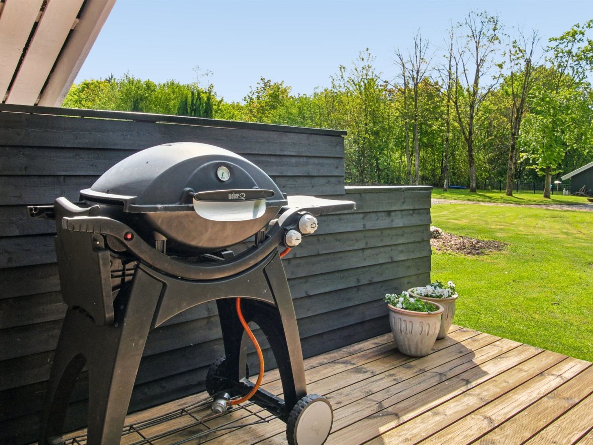 A Weber grill on a wooden deck with a green lawn and trees in the background.