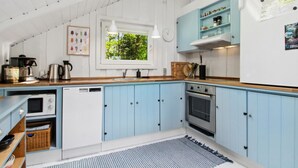 Une cuisine avec des meubles bleus, un lave-vaisselle, un four et une fenêtre donnant sur un paysage verdoyant.
