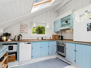Eine Küche mit blauen Schränken, einem Geschirrspüler, einem Backofen und einem Fenster mit Blick auf Grünflächen.