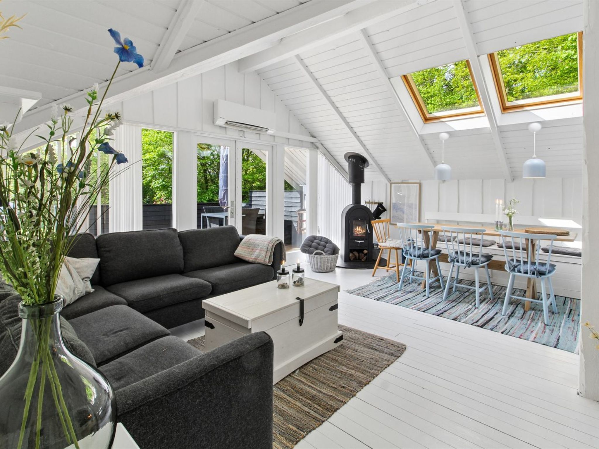 Ett modernt vardagsrum med en öppen spis, en soffa, en matplats och stora fönster.