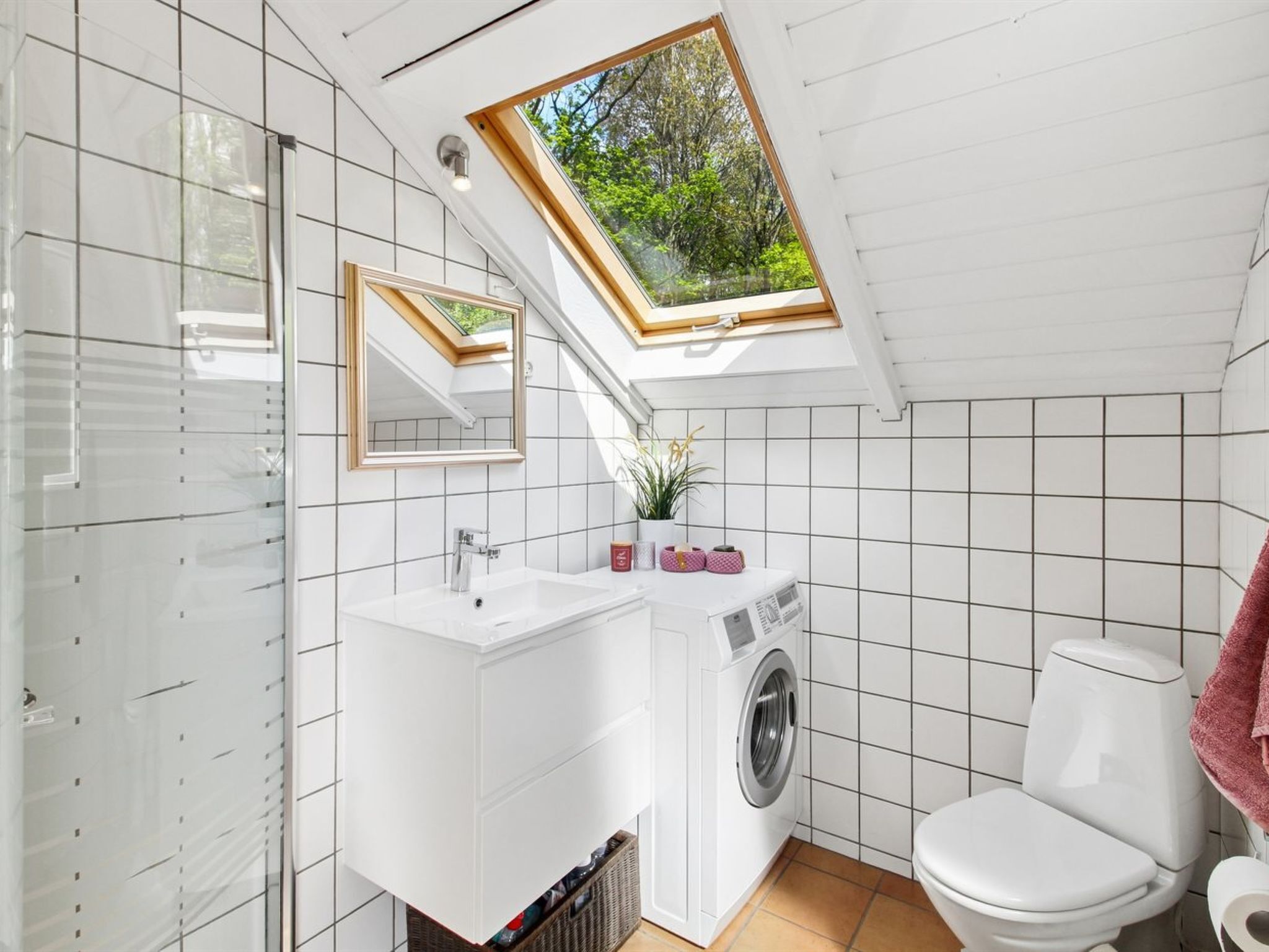 A compact bathroom with a skylight, a washing machine, and a toilet.