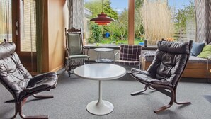 Een moderne woonkamer met lederen fauteuils, een ronde tafel en uitzicht op groen buiten.