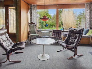 Un salón moderno con sillones de cuero, una mesa redonda y vistas al exterior con vegetación.