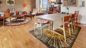Een moderne woonkamer met een bakstenen muur, houten plafond, een eettafel met stoelen, een bank en een vloerkleed.