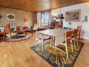 Una sala de estar moderna con pared de ladrillo, techo de madera, una mesa de comedor con sillas, un sofá y una alfombra.