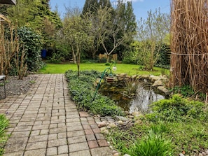 Un sendero de jardín que conduce a un estanque rodeado de follaje y una valla de madera.