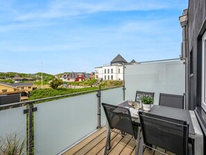 Un balcón con mesa y sillas, una planta en maceta y vistas a casas al fondo.