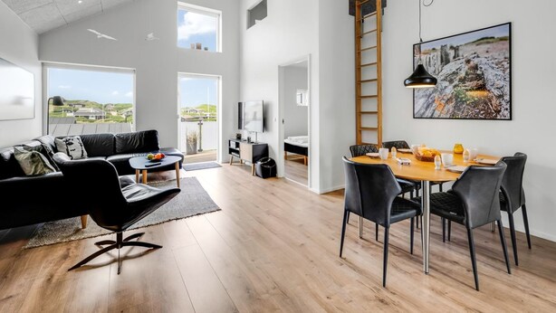 Un vaste espace de vie comprenant un canapé en cuir noir, une table à manger avec des chaises, un téléviseur et une grande fenêtre donnant sur l’extérieur.