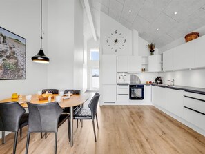 Een moderne keuken met witte kasten, een inbouwoven en een eethoek met een ronde tafel en stoelen.
