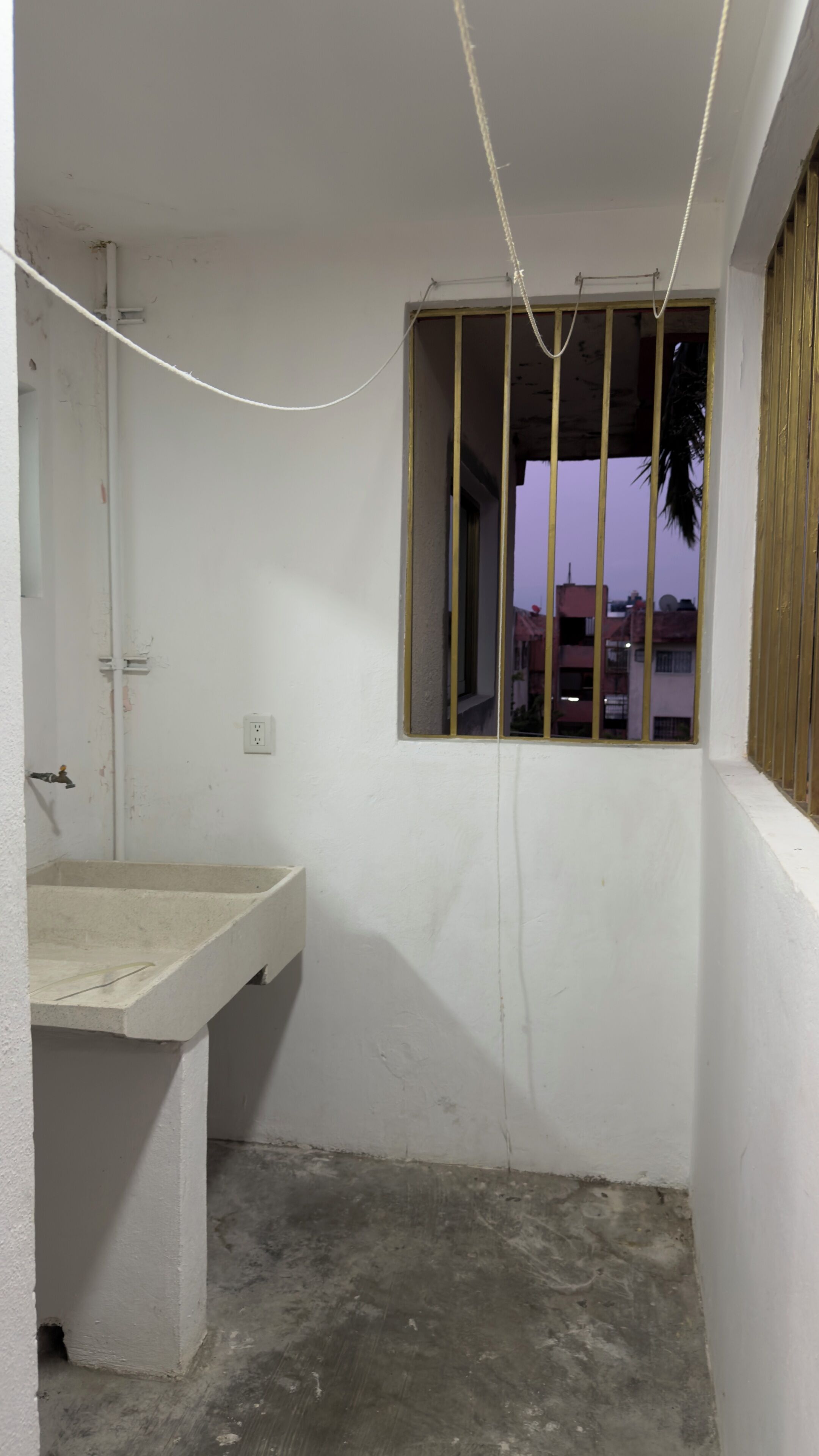 Una habitació amb un rentanau de formigó, una finestra amb reixes metàl·liques i una presa elèctrica visible.