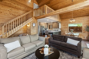 A wooden interior with a staircase, two sofas, a dining table, and a kitchen area.