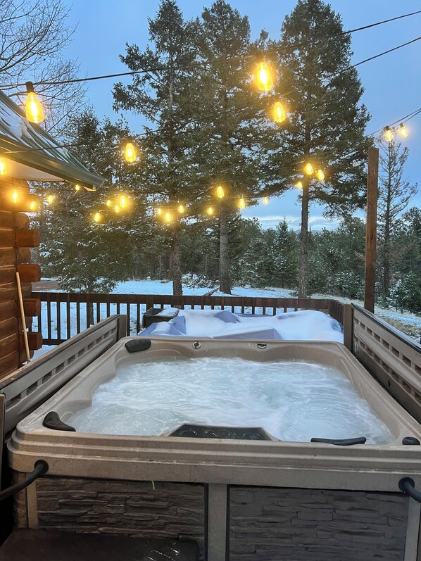 Ein Whirlpool mit Steinverkleidung, umgeben von einer Holzterrasse und schneebedecktem Boden.