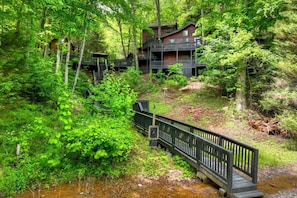 Eine Holzhütte mit mehreren Terrassen, umgeben von dichtem Wald und einem kleinen Bach.