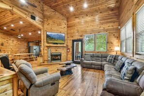 Ein Blockhaus-Interieur mit Kamin, Fernseher und einer Couch.