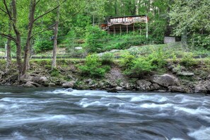 A river with a wooden bridge and a building with a deck.