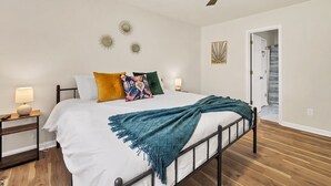 A bedroom with a bed, a ceiling fan, bedside lamps, and a door leading to a bathroom. - Lake Life Chapin Retreat, Sleeps 7, King Bed (Chapin)