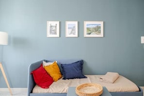 Een kamer met een blauwe wand, een bank met kussens, een kleine tafel en drie ingelijste foto's.