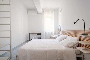 Une chambre d’hôtel moderne, équipée d’un lit, de tables de chevet, d’un bureau, d’une lampe, d’une fenêtre avec des rideaux et d’une armoire blanche.