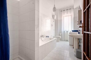 Ein modernes Badezimmer mit weißen Fliesen, einer Badewanne, einer Toilette und einem Waschbecken.