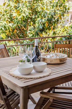 Une table en bois, sur laquelle se trouvent deux bols, une bouteille et un récipient rempli de petits cailloux, est placée sur un balcon d’où l’on peut admirer la verdure.