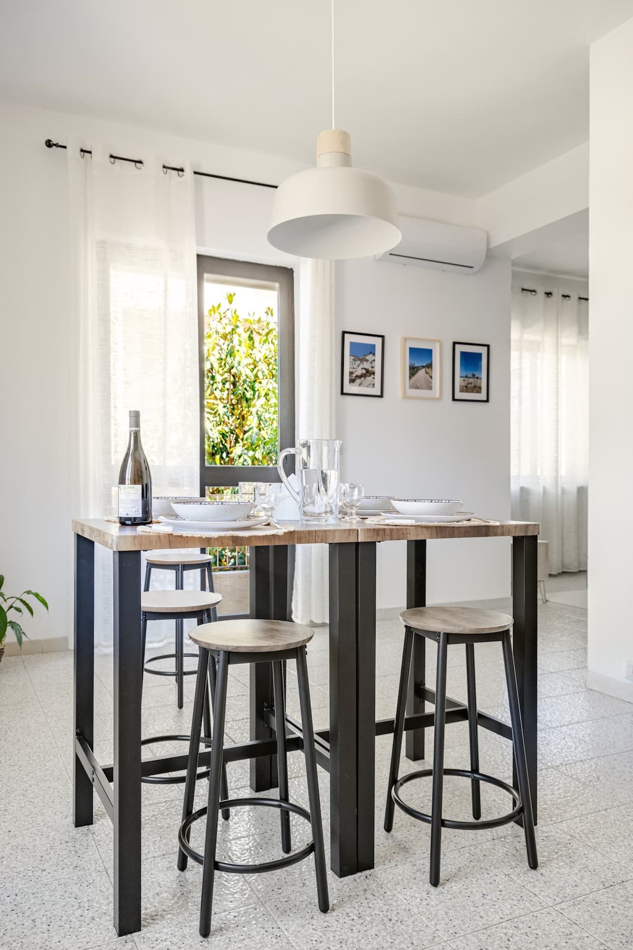 Un espace repas comprenant une table, des tabourets, un luminaire suspendu et une fenêtre donnant sur un paysage.