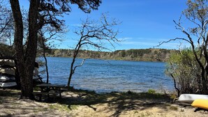 En campingplads ved søen med borde-bænkesæt, en kano og en stabel stole.