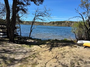 A lakeside camping area with picnic tables, a canoe, and a stack of chairs. - New! Luxury Home near town, beach, and private lake access! (Chatham)
