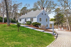 A two-story house with a sloped roof, a front porch, and a paved driveway. - New! Luxury Home near town, beach, and private lake access! (Chatham)