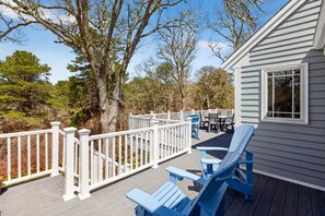 A deck with blue Adirondack chairs, a table, and a white railing. - New! Luxury Home near town, beach, and private lake access! (Chatham)