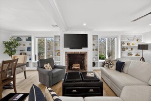 A living room with a fireplace, a television, and a bookshelf. - New! Luxury Home near town, beach, and private lake access! (Chatham)