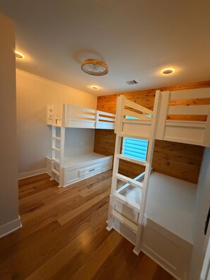 Ein Zimmer mit Etagenbetten, Holzboden und eingelassenen Deckenleuchten.